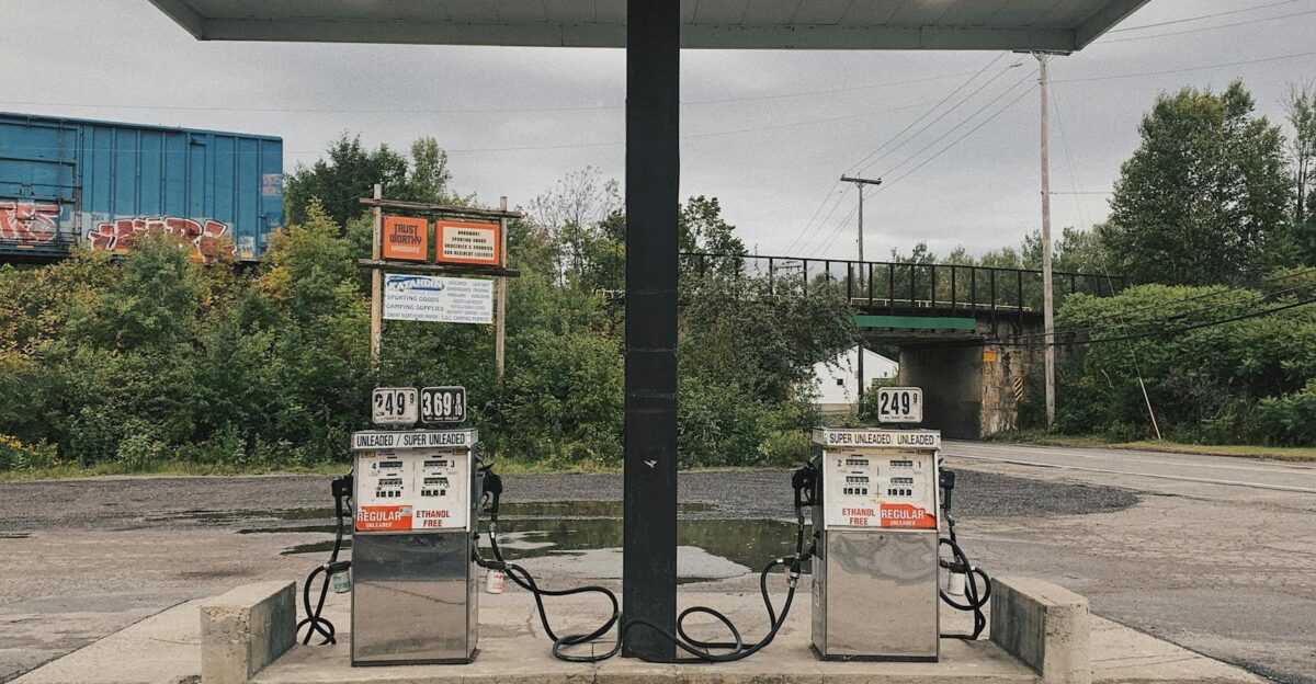 An outdoor scene of an abandoned gas station with dual pumps and vivid greenery in the background