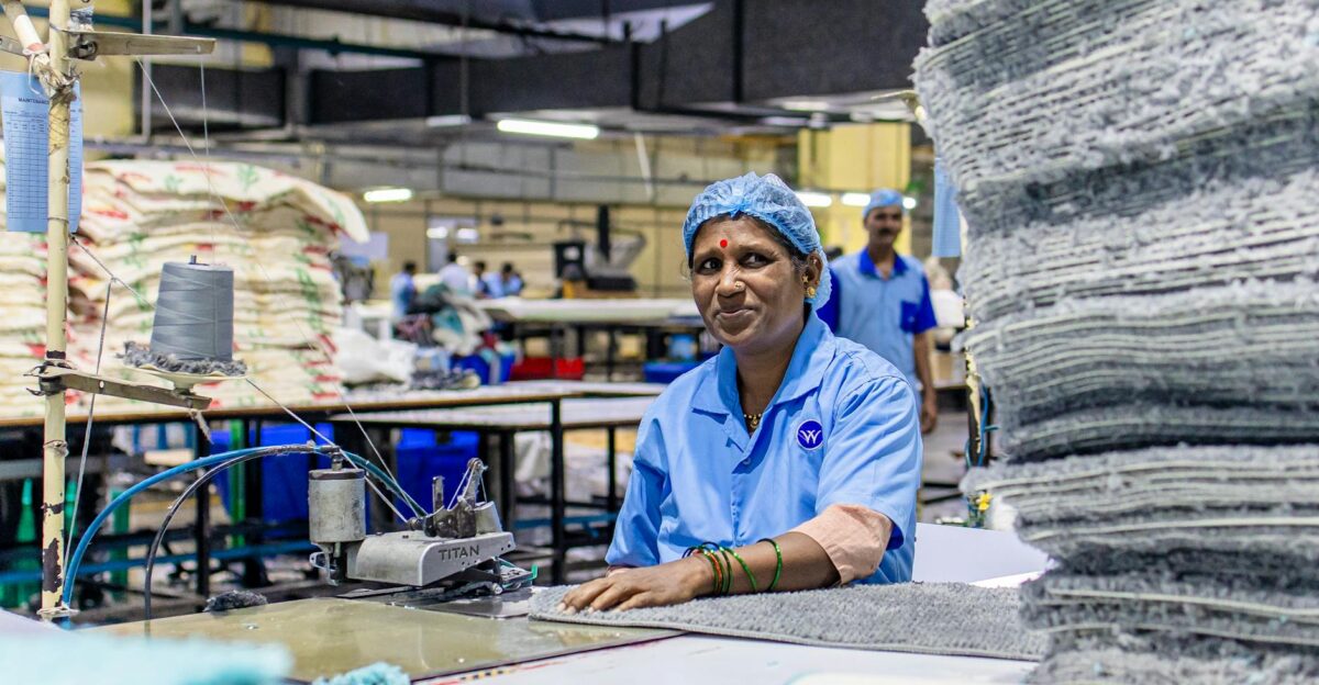 An Indian textile worker in blue uniform smiling at a textile factory