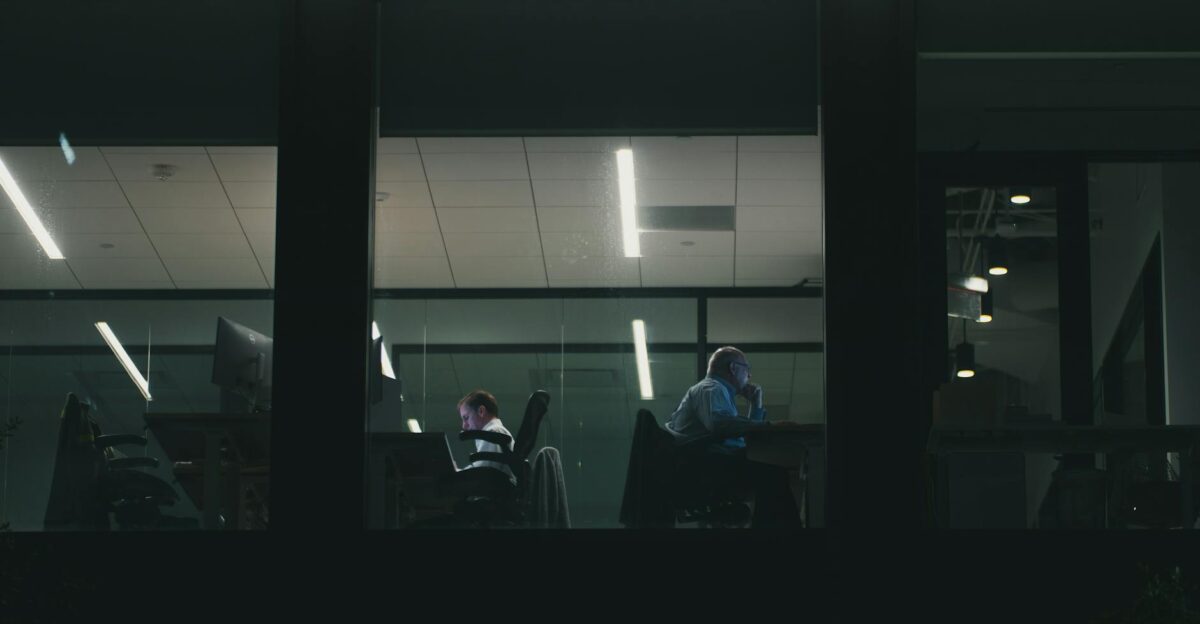 Two people working late in a modern Houston office building visible through a window