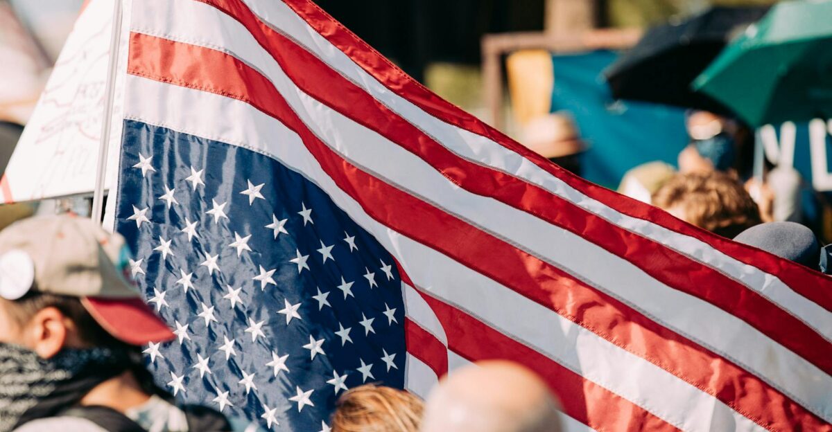 Close-up of an American flag waving at a public gathering with people in the background