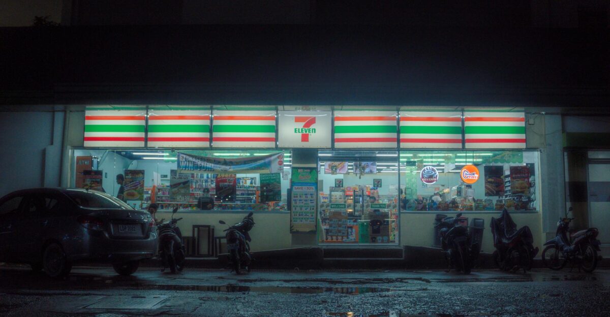 Moody nighttime scene of a 7-Eleven store with parked vehicles and reflections