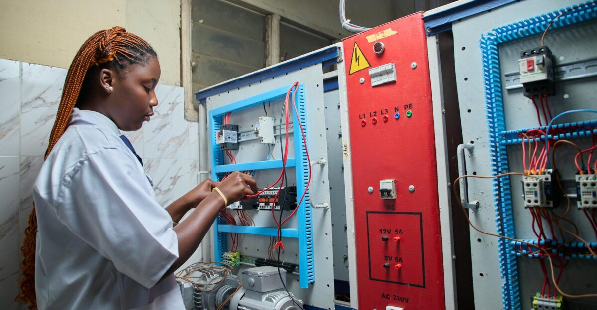 Young female technician repairing electrical control panel in industrial setting