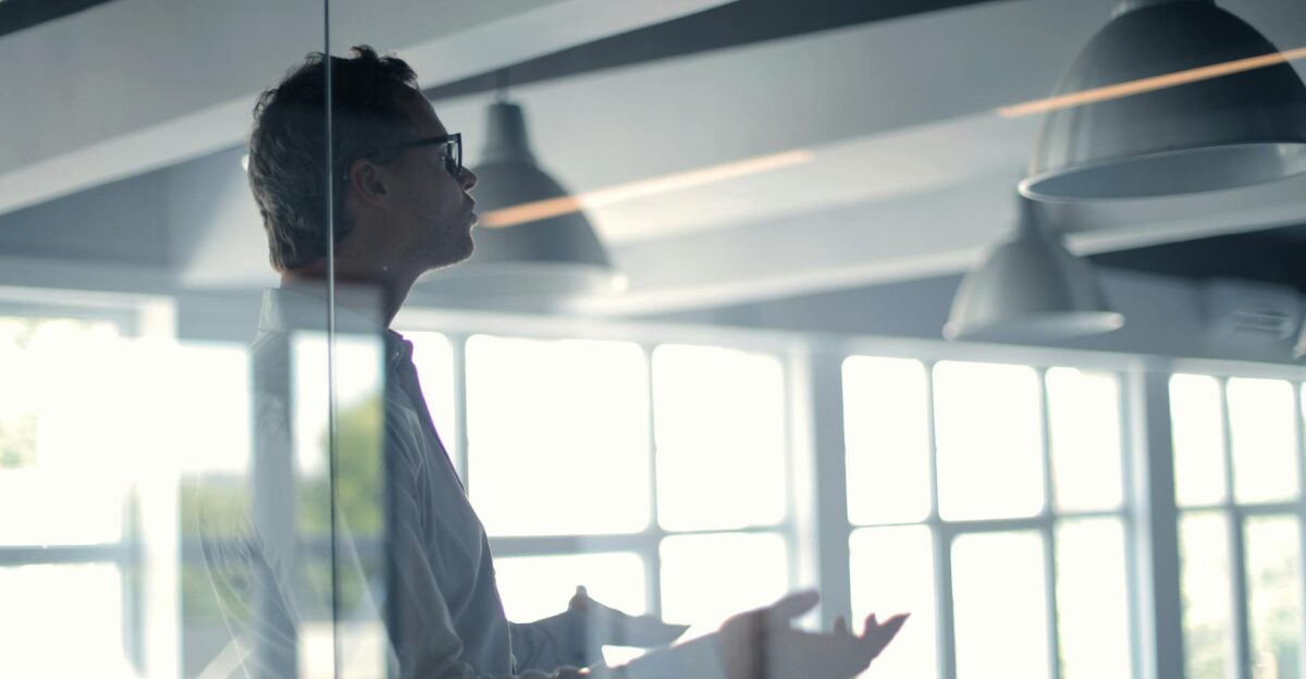 Business professional giving a presentation in a modern office setting through glass
