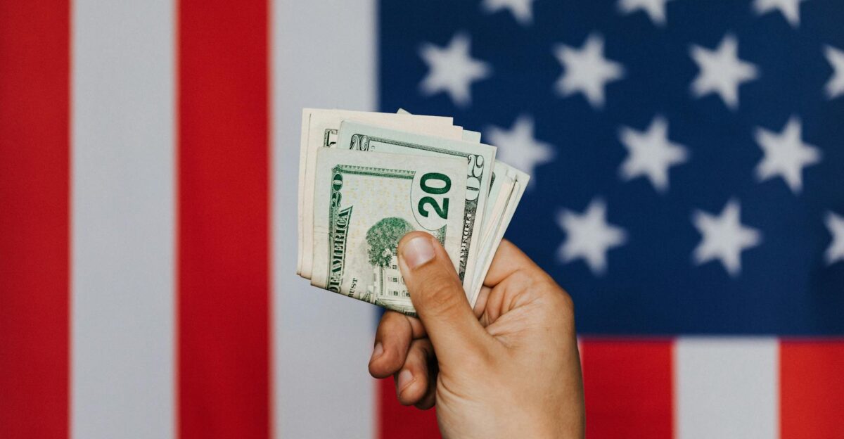 Unrecognizable male demonstrating dollars before official flag of USA on background