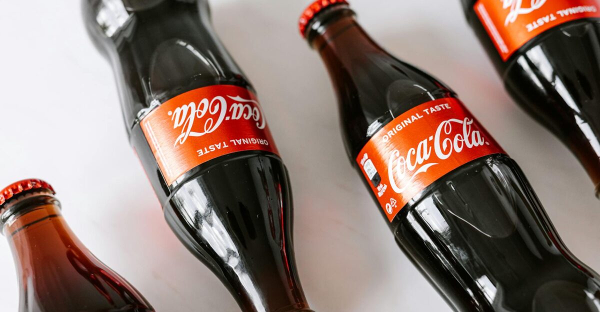From above of glass bottles full of soft coke drink placed on white background