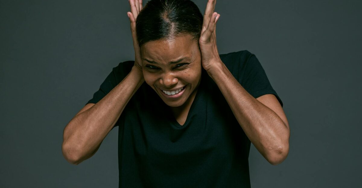 Portrait of an adult woman covering ears looking irritated against a dark background