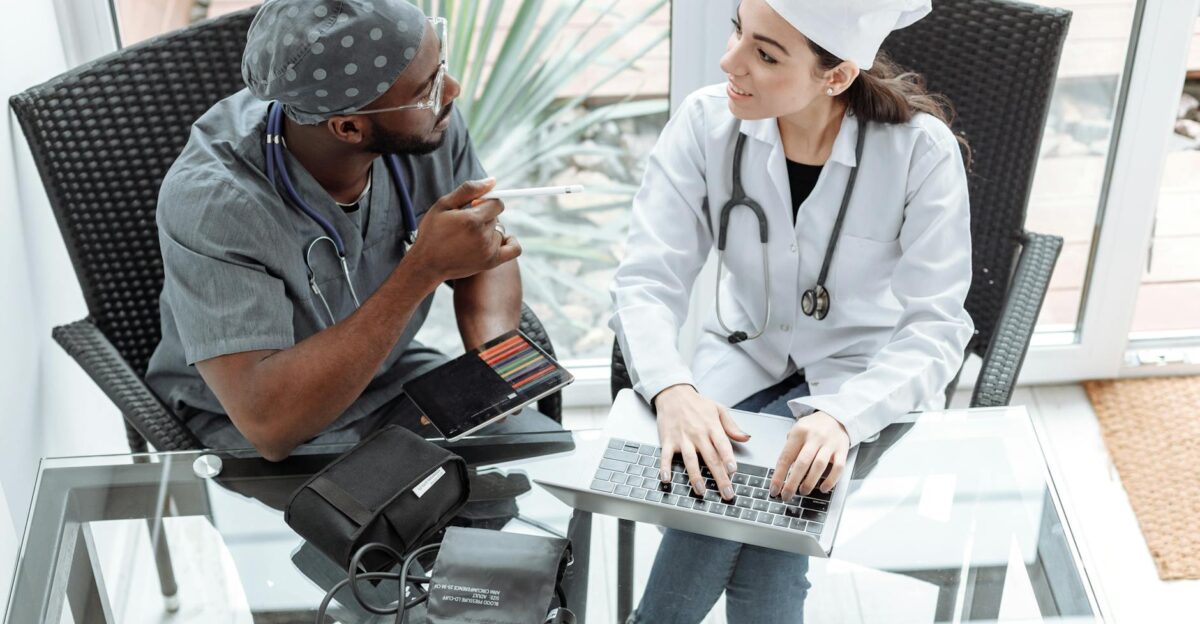 Two doctors discussing patient care using a laptop and tablet indoors