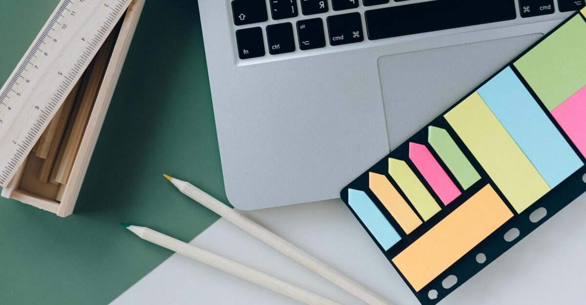 Organized desk with a laptop sticky notes pencils and a ruler on green and white surface