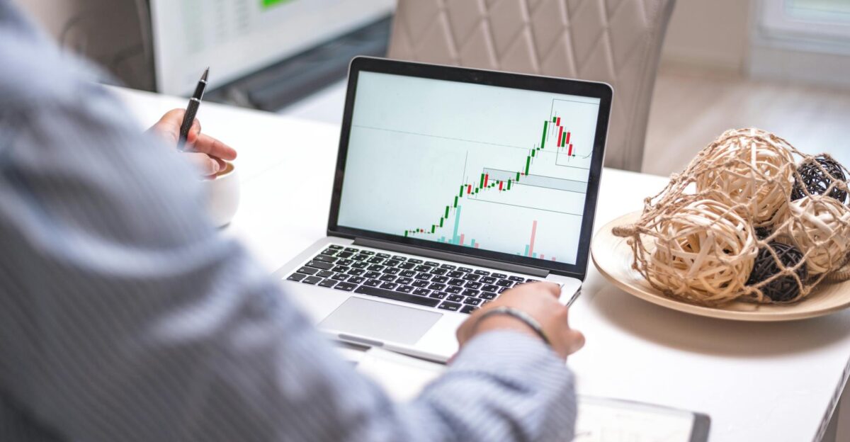 Person analyzing stock market trends on laptop in a modern home office setting