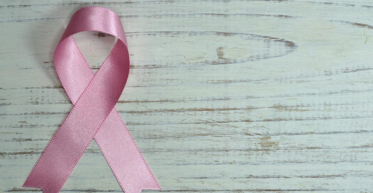 A pink ribbon symbolizing cancer awareness placed on a light wooden background