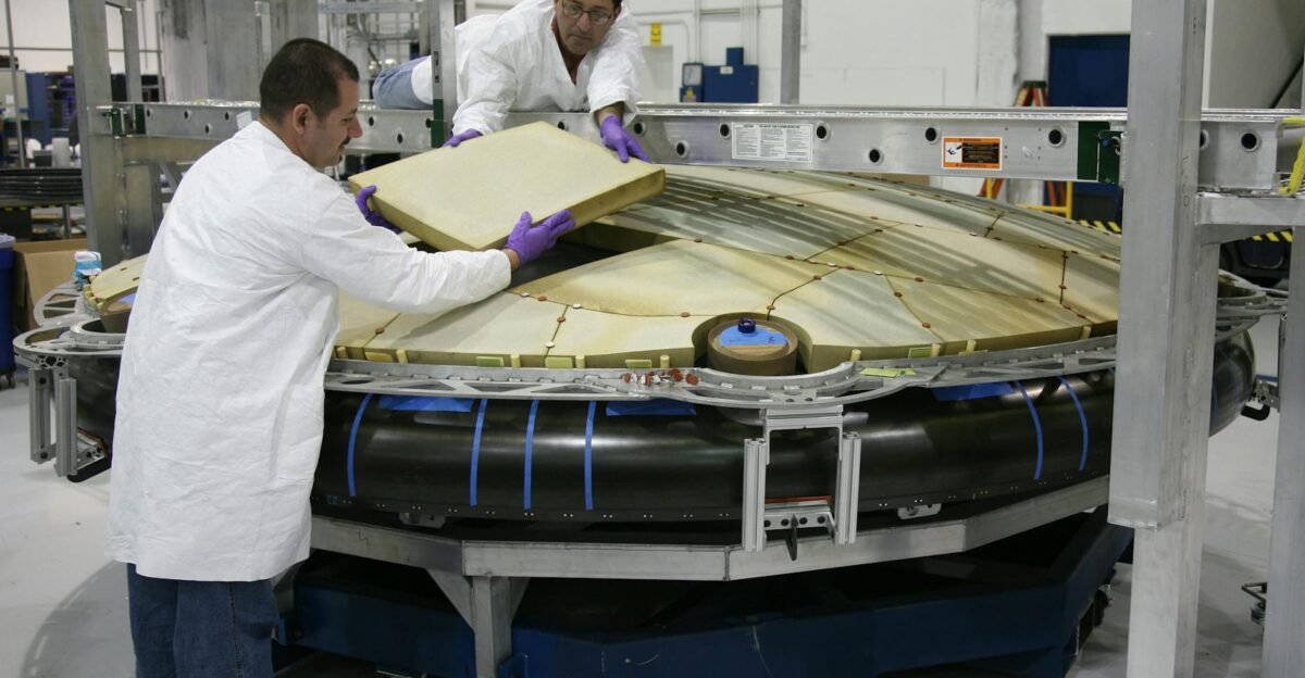 Technicians work diligently to assemble a spacecraft part in a modern industrial facility
