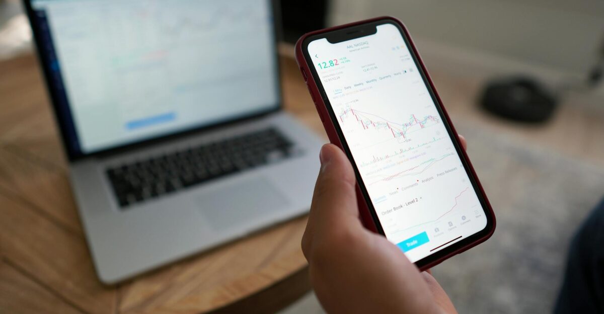 A person trading stocks on a smartphone and laptop Ideal for finance themes