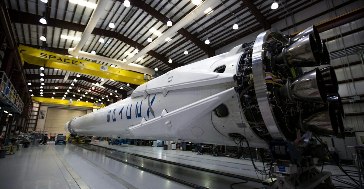 A SpaceX Falcon rocket displayed in a spacious hangar under bright industrial lights