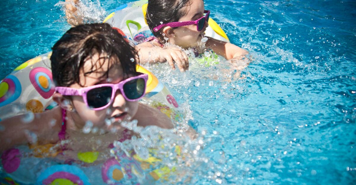 Two young girls enjoying a playful day in a bright blue swimming pool with colorful float rings