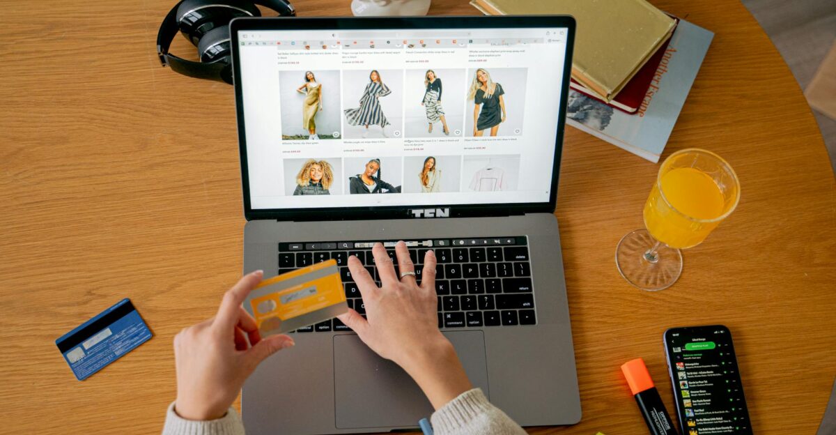 Hands holding credit card making online purchase on laptop at wooden desk with various items