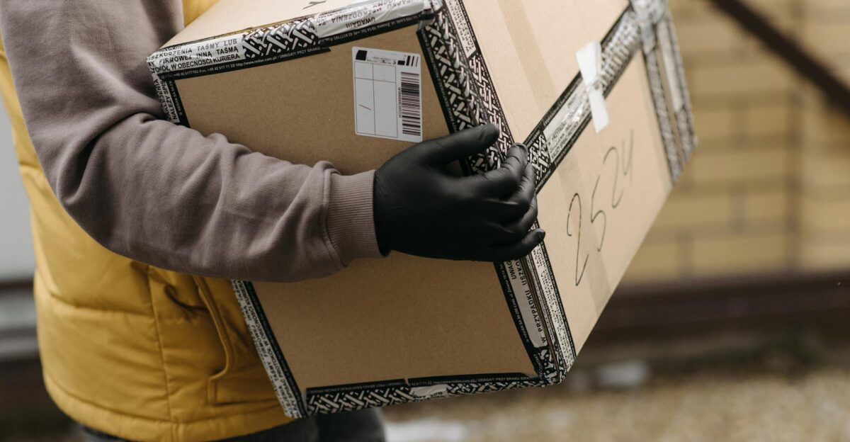 Courier holding a package marked TOP PACKAGING wearing gloves for safe delivery