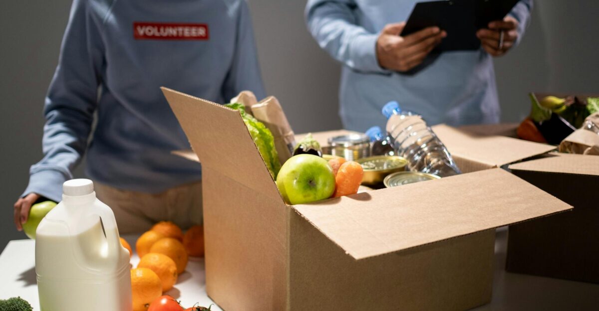 People packing a cardboard box with essentials like fruits vegetables and bottled water for charity