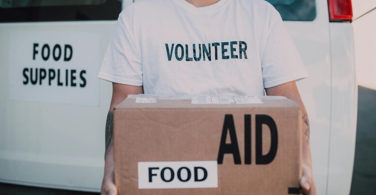 A volunteer holding a food aid box in front of a supply vehicle ready for distribution