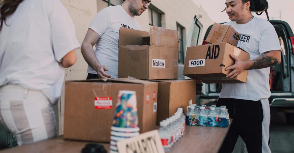 Volunteers loading aid boxes with food and medicine from a van outdoors