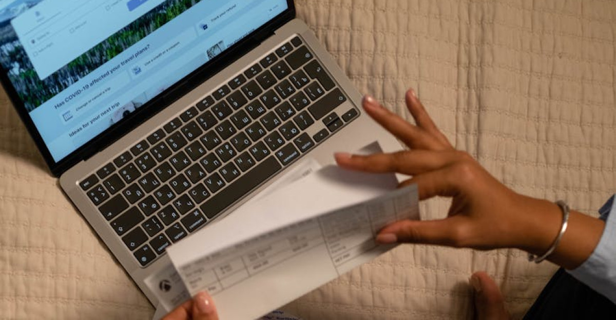 Woman holding checks while managing finances on a laptop showing online banking on the screen