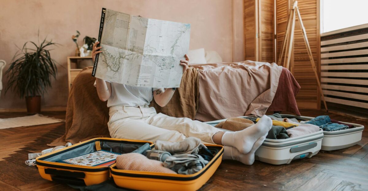 Person packing suitcases with a map in a cozy bedroom preparing for a journey