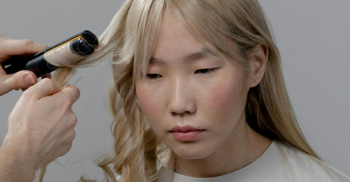 A hairstylist using a curling iron to style a woman's hair in a salon setting.
