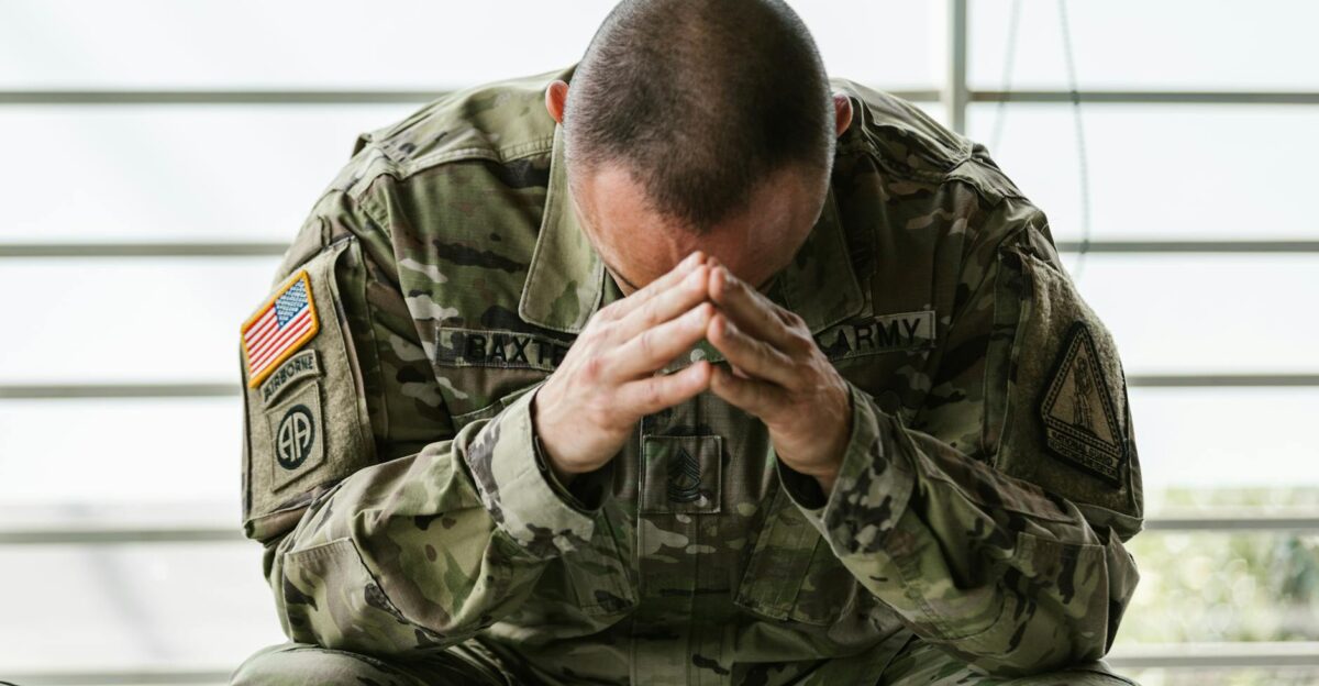 A soldier in camouflage sitting indoors appearing stressed and overwhelmed