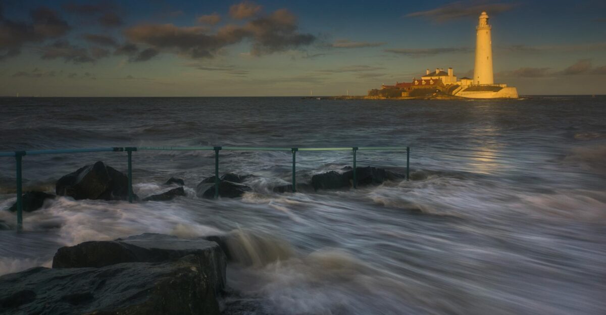 Breathtaking view of waves crashing against rocks with a lighthouse in the background at twilight