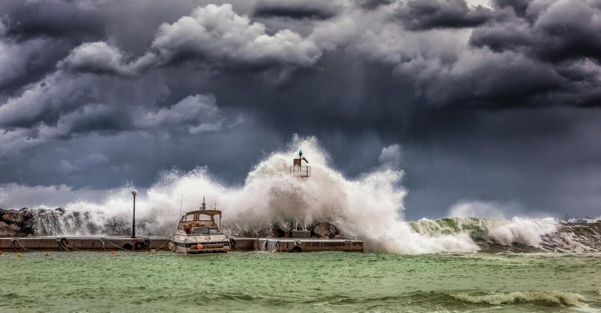 Powerful waves crash against a pier and lighthouse under dark stormy skies