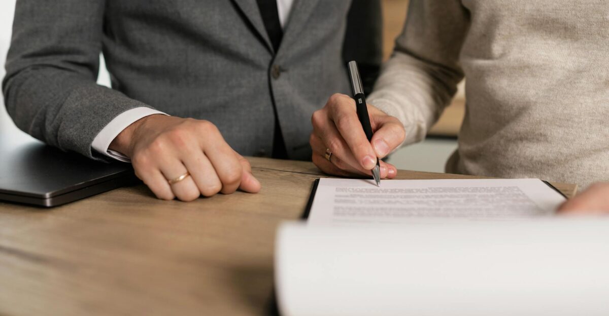 Close-up of businessmen signing documents at a wooden table in an office