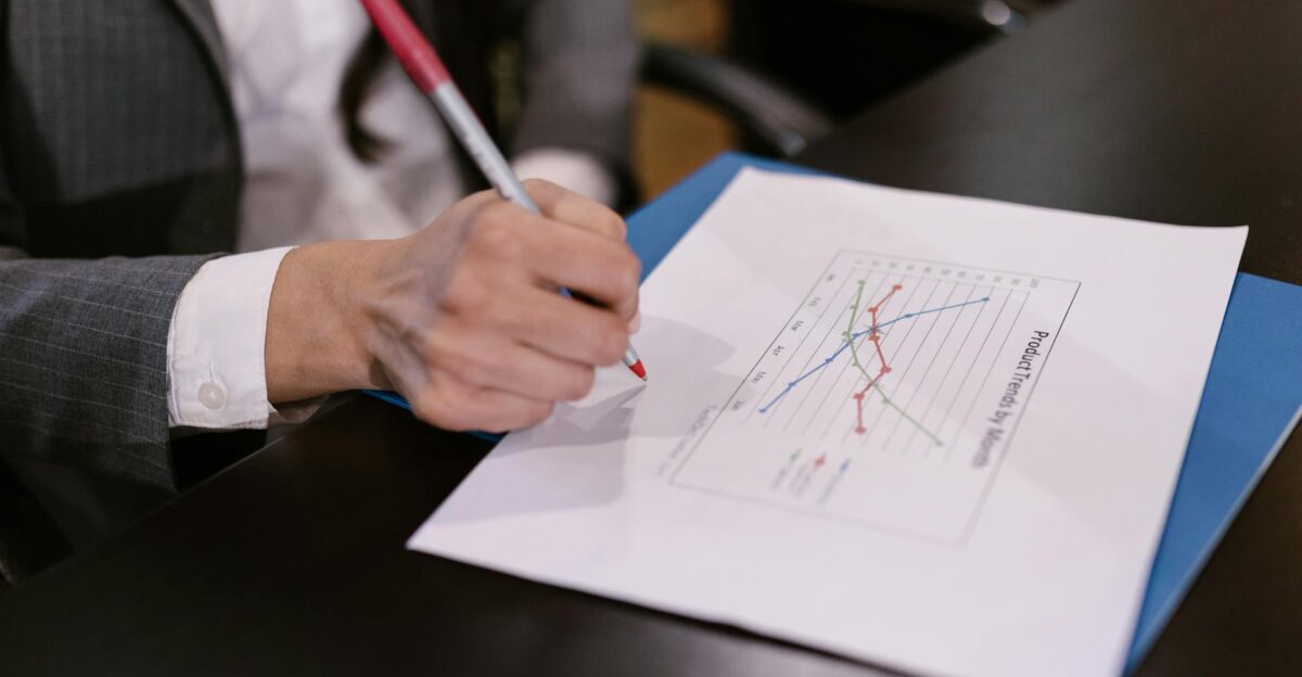 Close-up of a businesswoman holding a pen analyzing a graph report at a desk