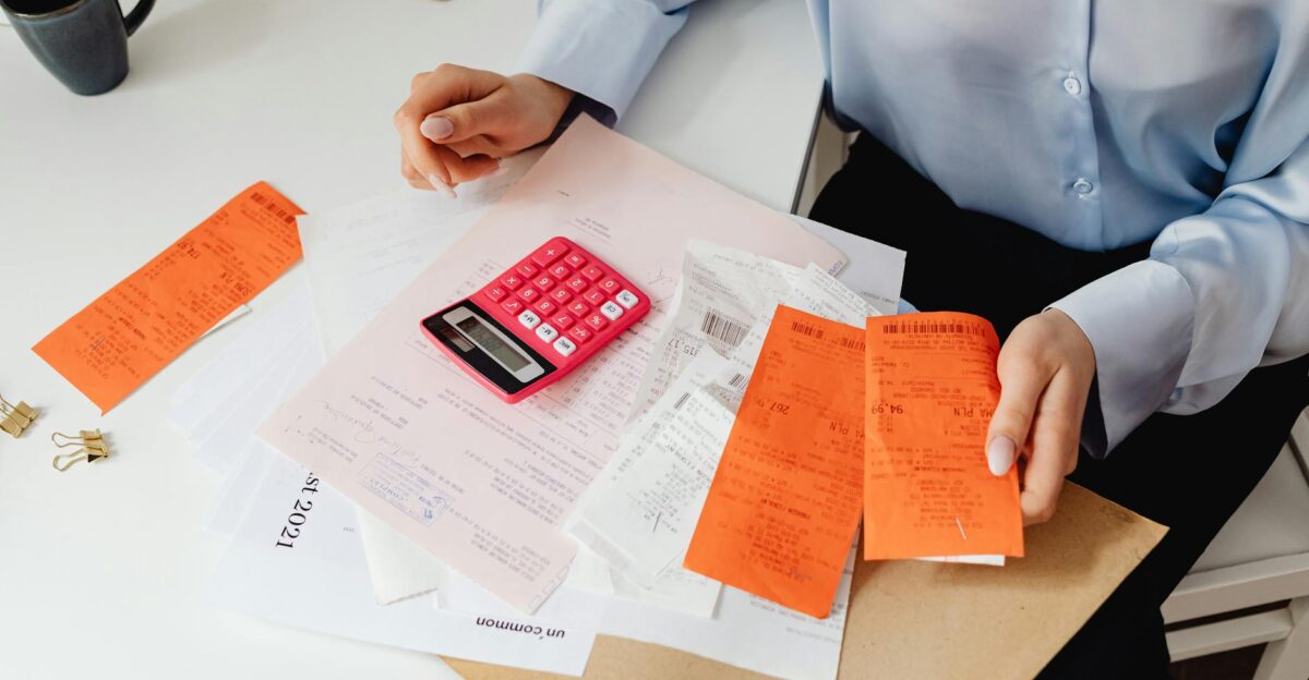A woman reviews receipts and calculates expenses at a desk with a pink calculator