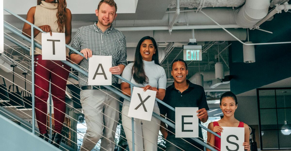 A diverse group of professionals smiling and holding TAXES signs on an indoor stairway
