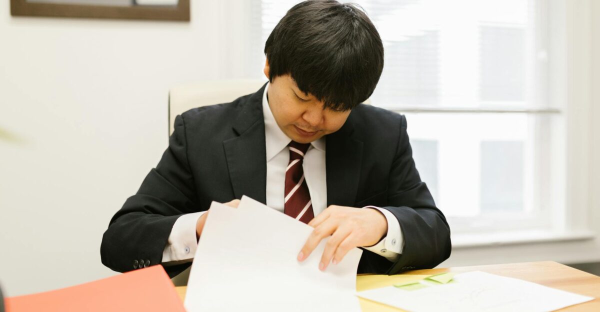 Businessperson in a suit examines papers at a desk indoors focused and diligent