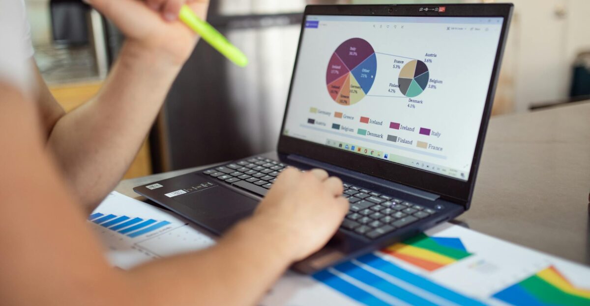 Person analyzing financial charts and graphs on a laptop with colorful documents showcasing market analysis