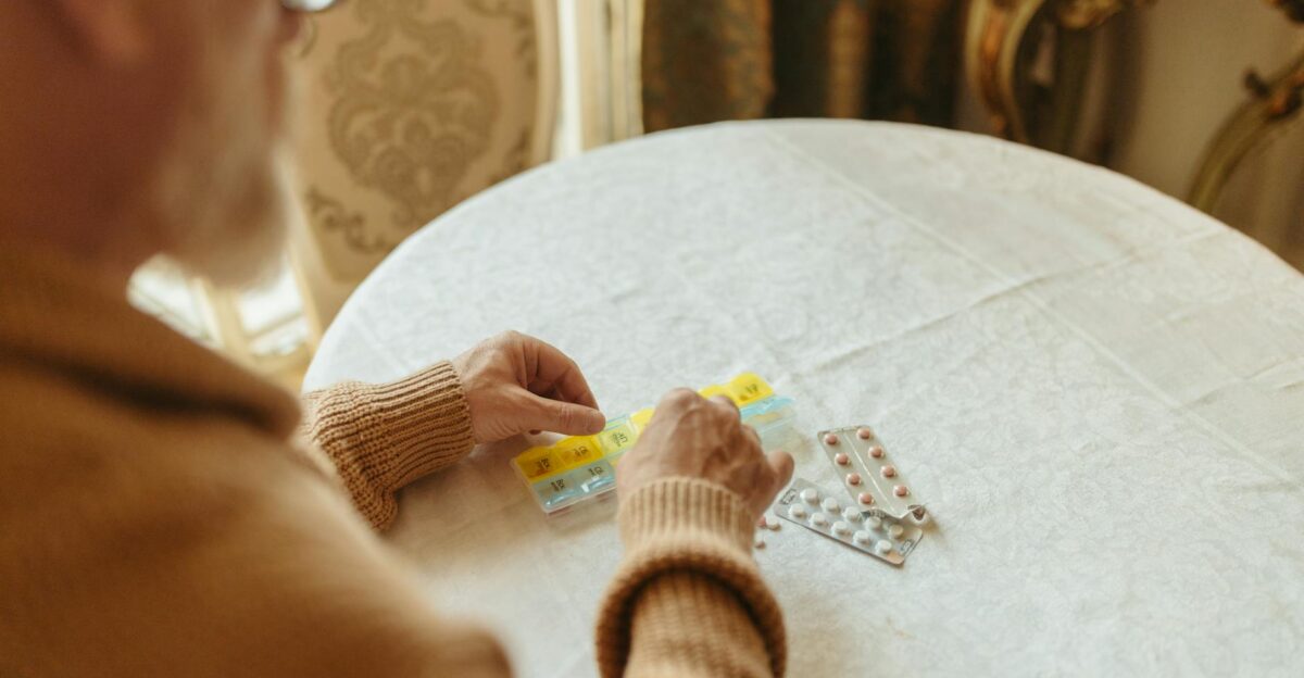 Elderly person sorting daily medication with a pill organizer on a table indoors