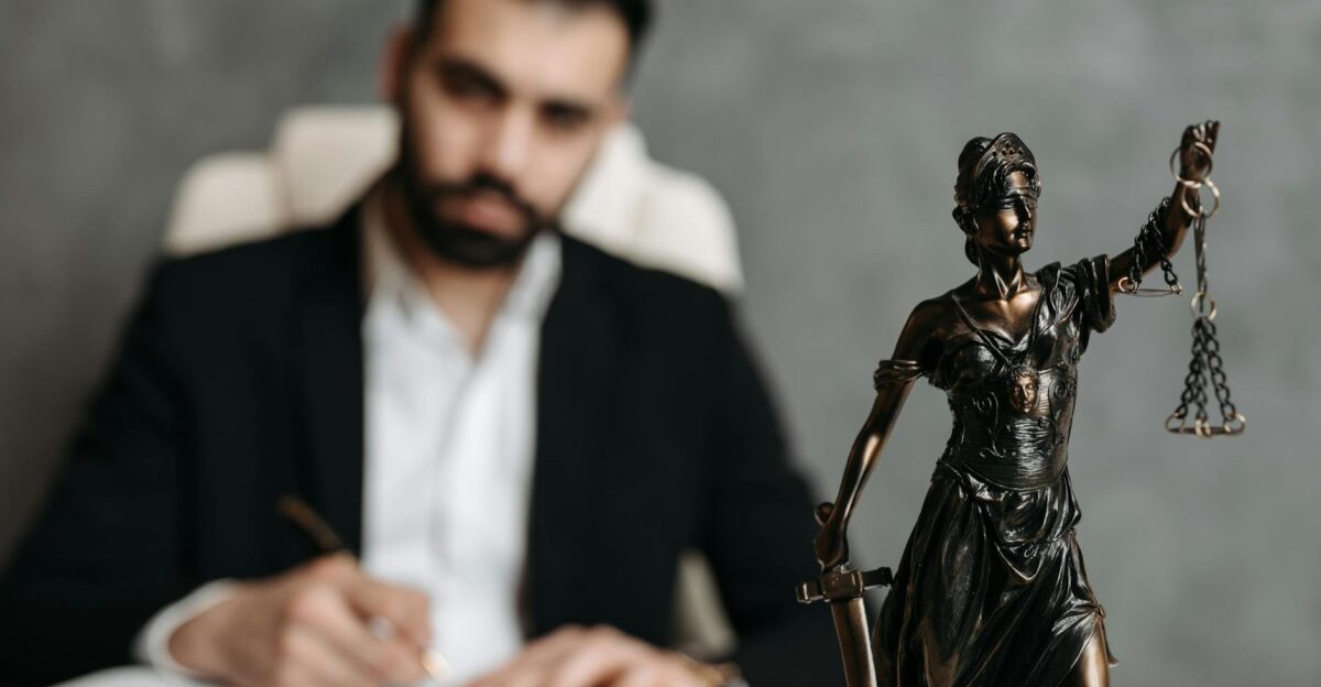 A lawyer in a suit writes at a desk with a Lady Justice statue in the foreground