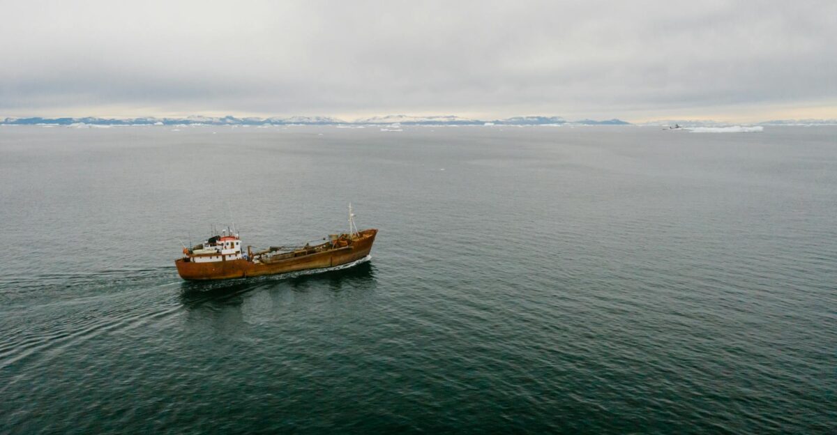 An aerial view of a rustic ship sailing on expansive calm ocean waters