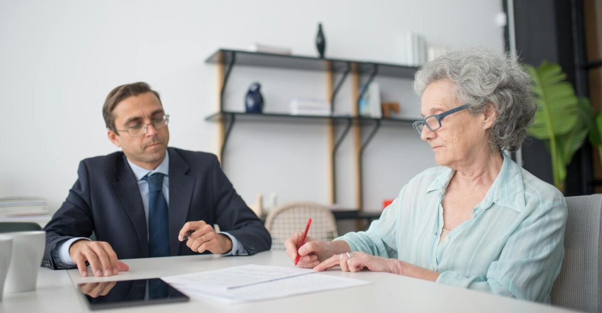 Elderly woman signing paperwork in modern office with consultant