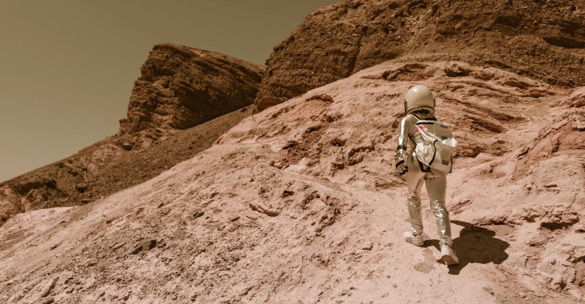 Astronaut in a space suit walking uphill on a rocky desert-like alien planet