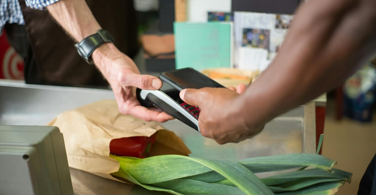 A customer making a contactless payment with a smartphone at a grocery store checkout counter