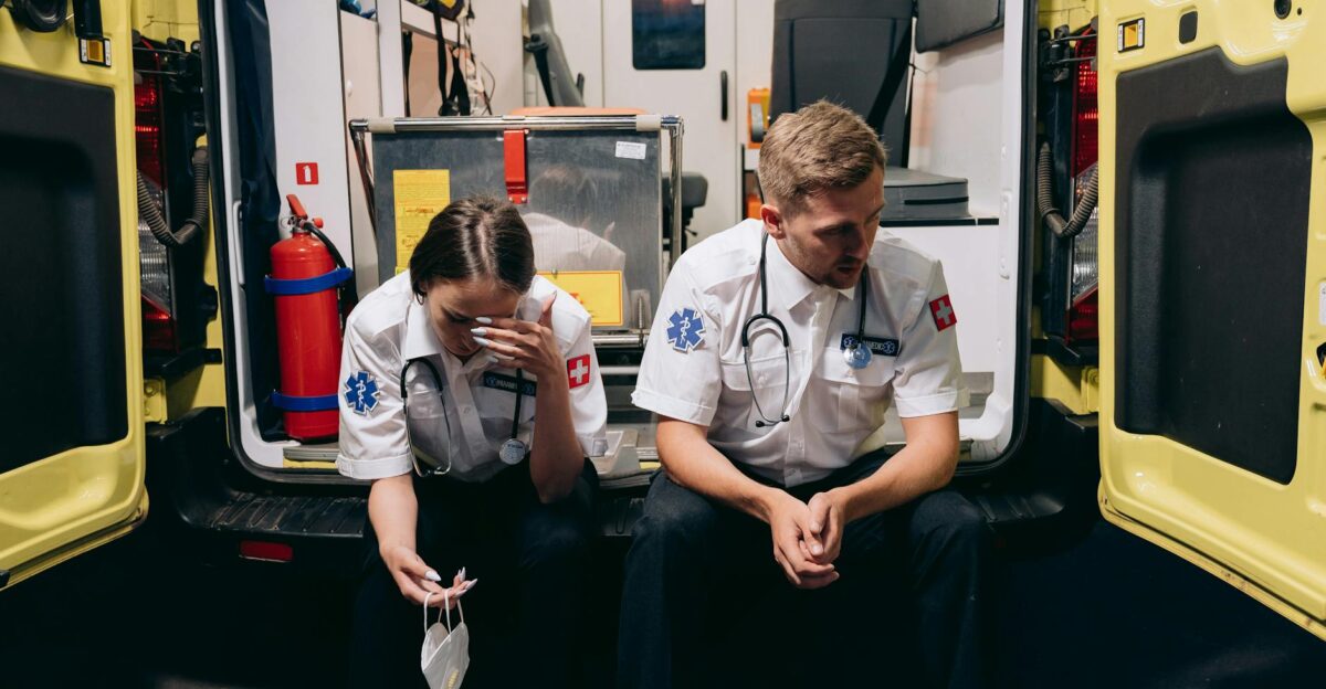 Two paramedics sitting tired at the back of an ambulance reflecting the stress of emergency services