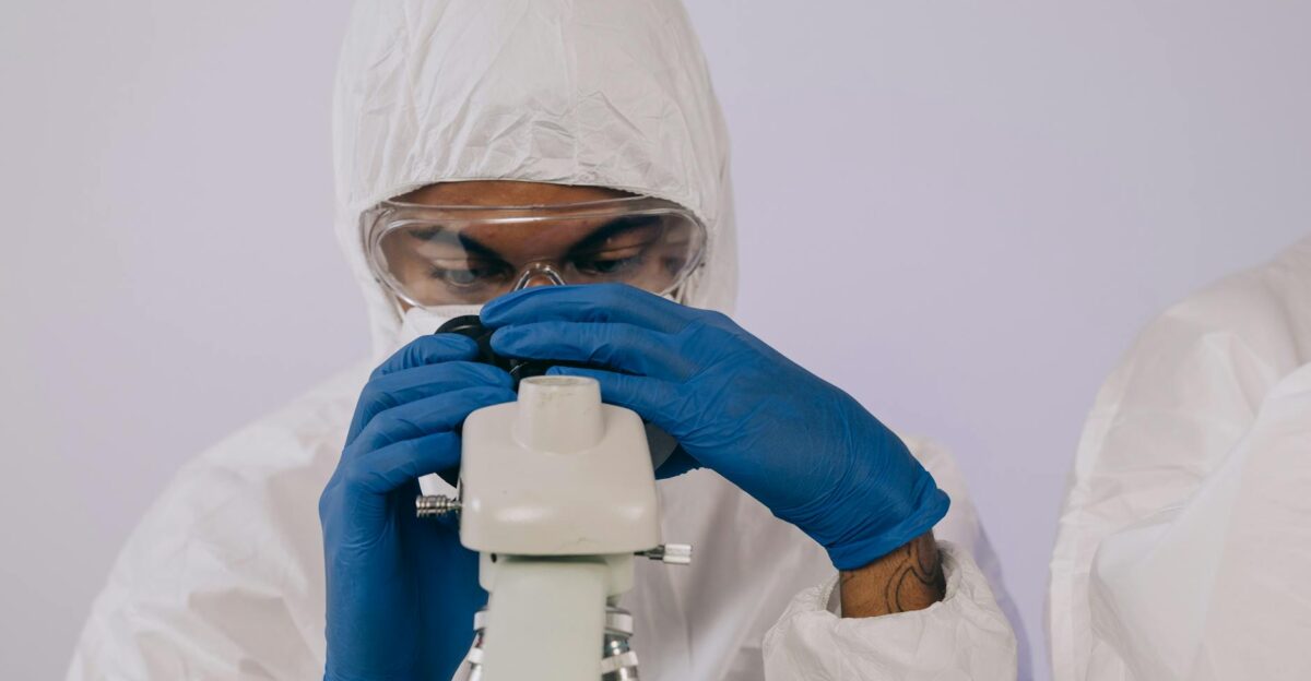Scientist in protective gear examines samples through a microscope in a lab setting