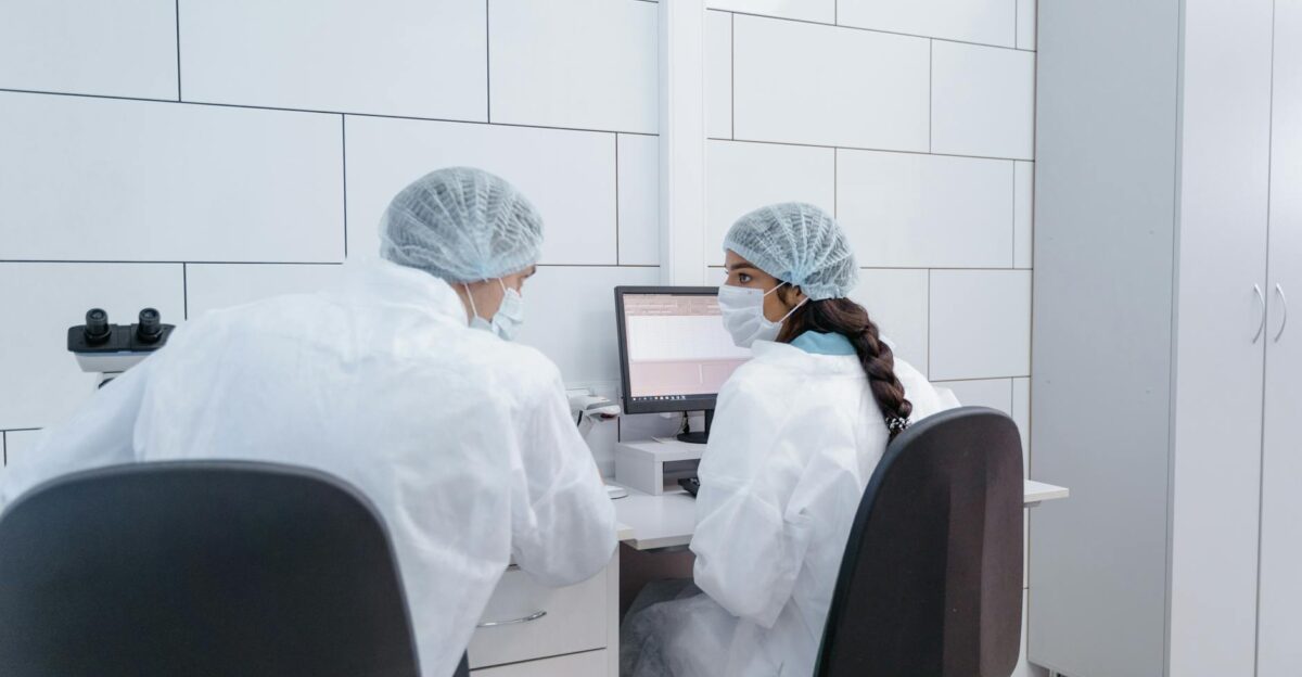 Two scientists in PPE discussing research at a computer in a laboratory setting