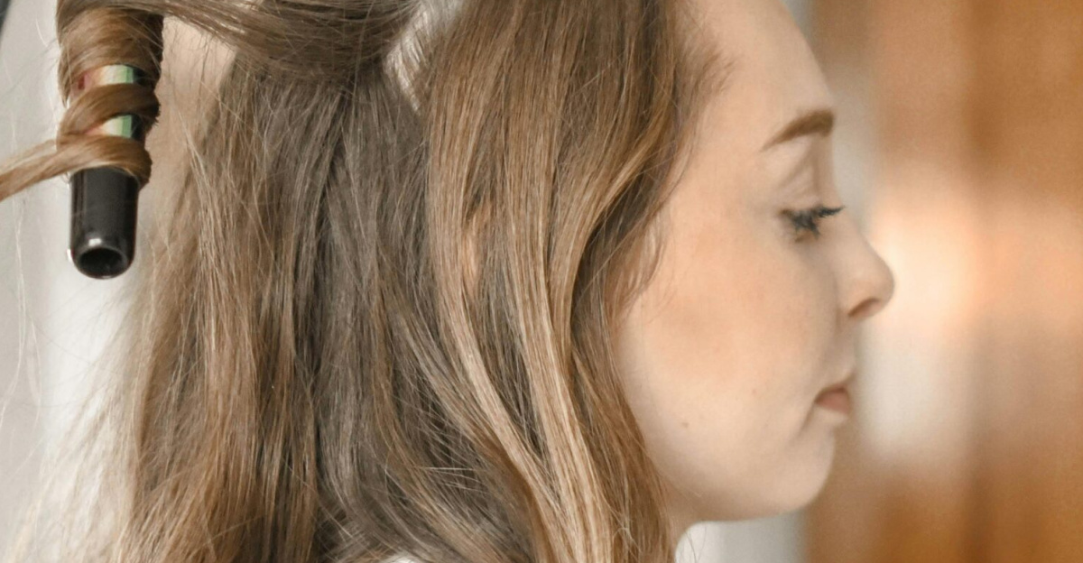 Profile of a woman having her hair curled with an iron in a salon setting.