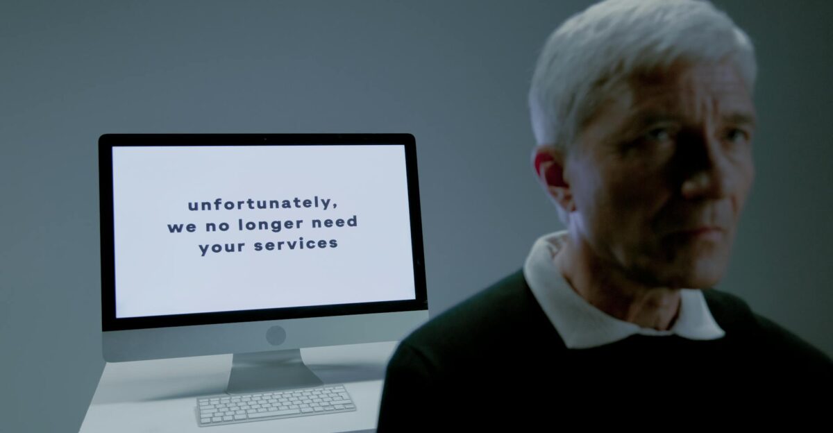 Senior man looks away from an unemployment notice on a computer screen indoors