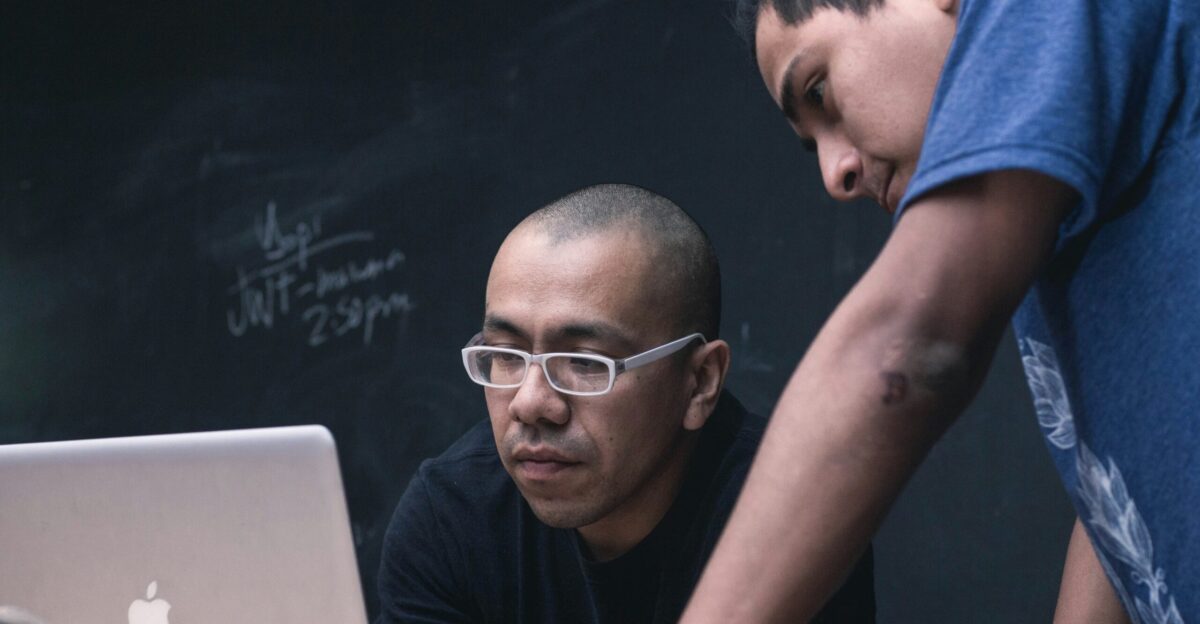 two men watching on silver MacBook