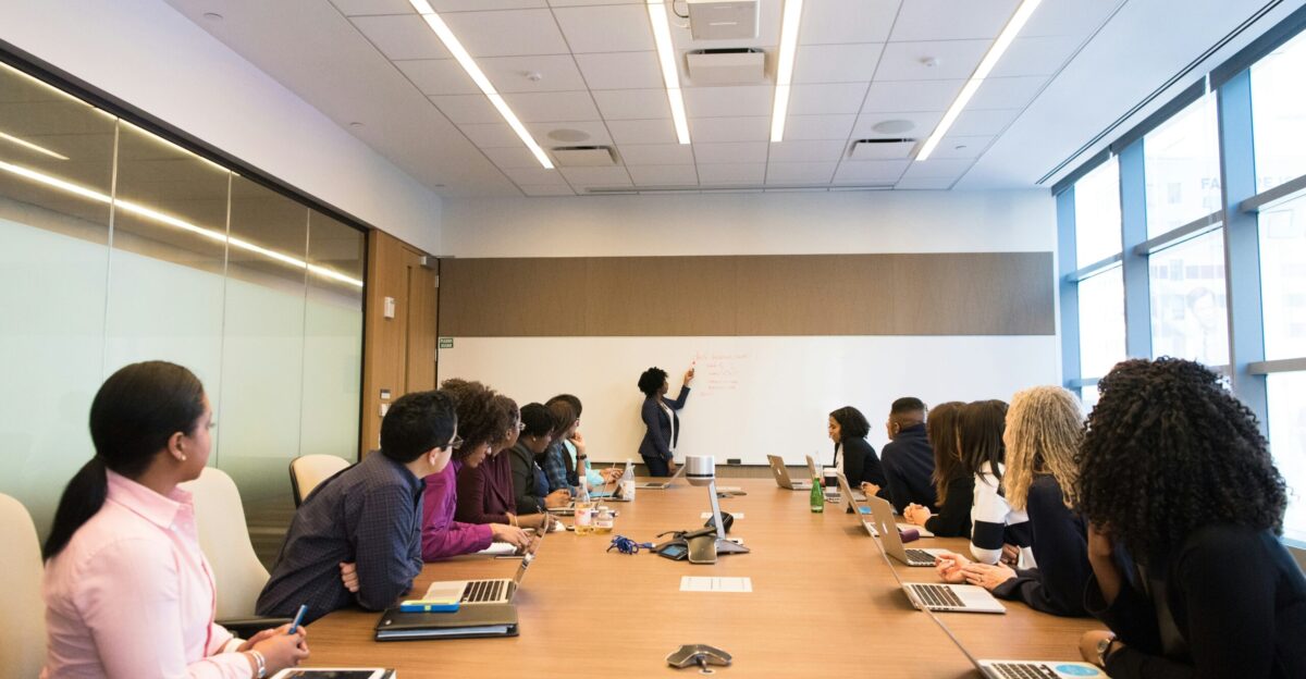 people on conference table looking at talking woman