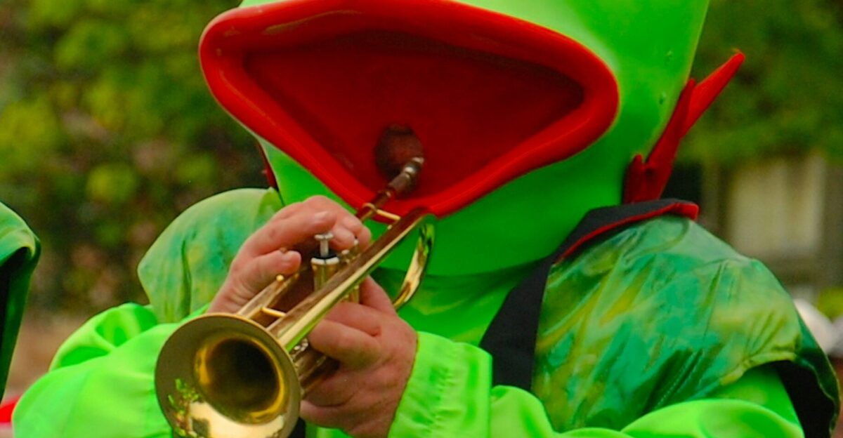 person in frog costume while playing trumpet