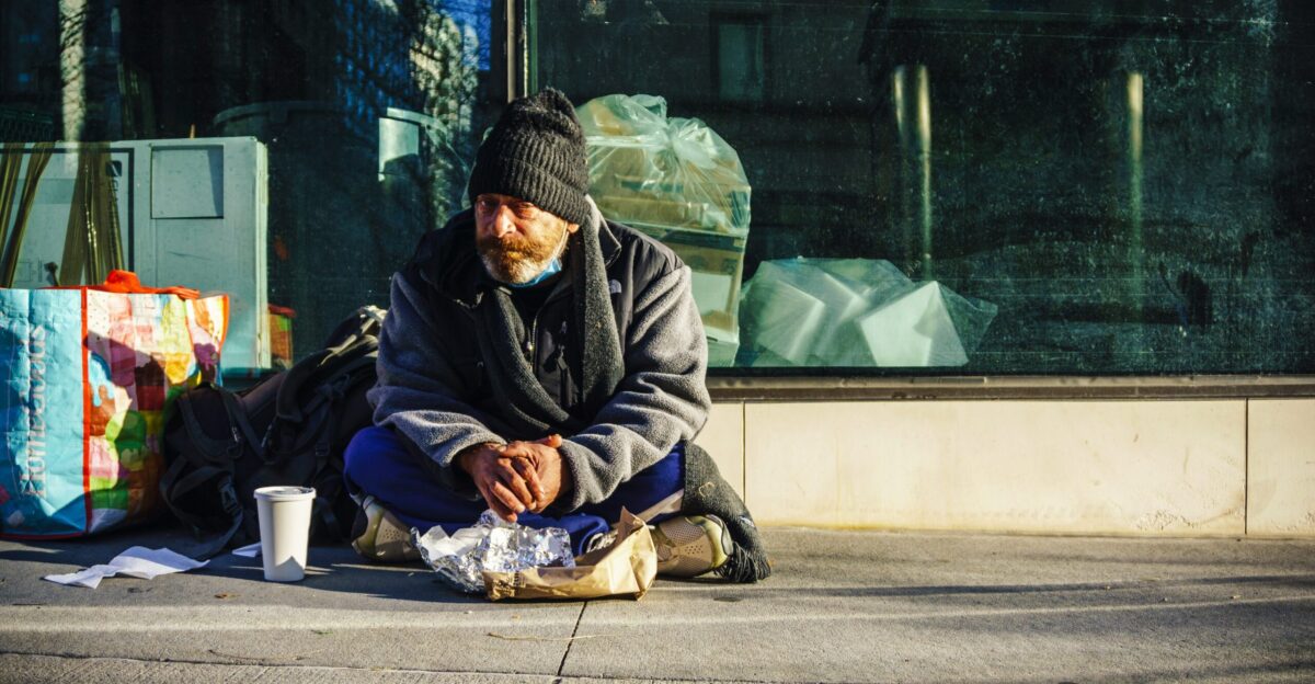 man in black and gray jacket sitting on sidewalk during daytime